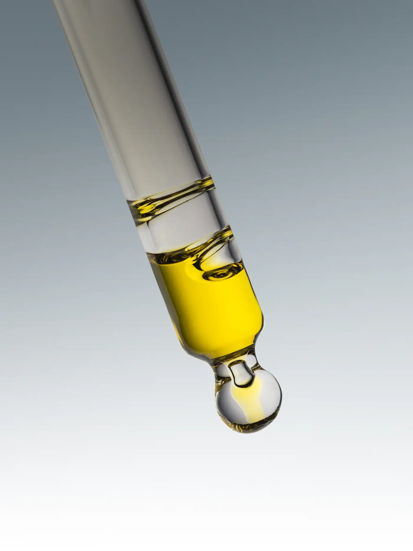 A golden drop of oil falling from a pipette
