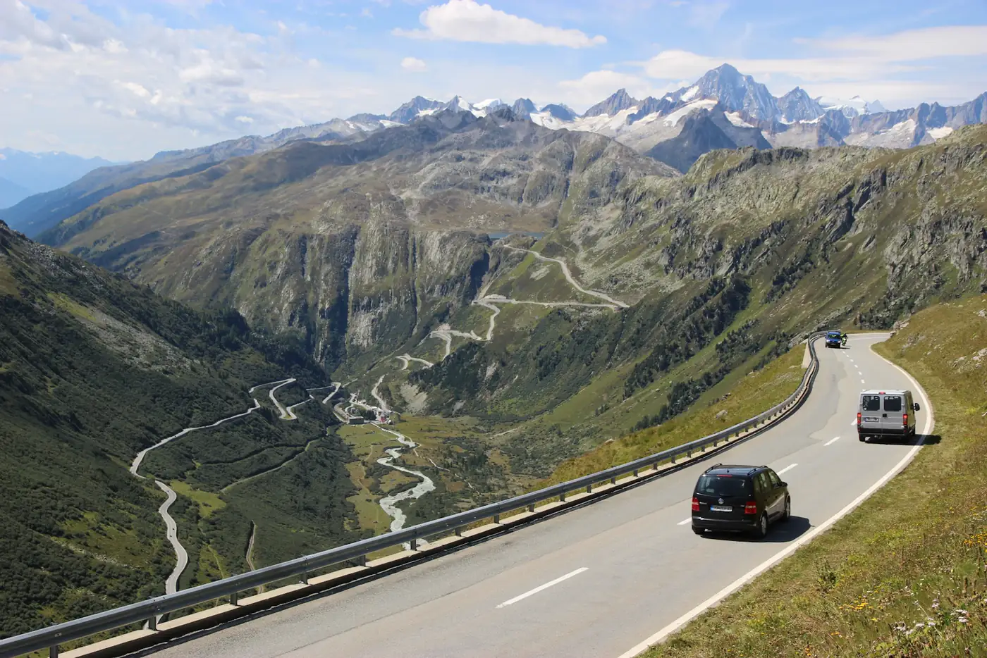 A car climbing a mountain switchback road below snowy peaks