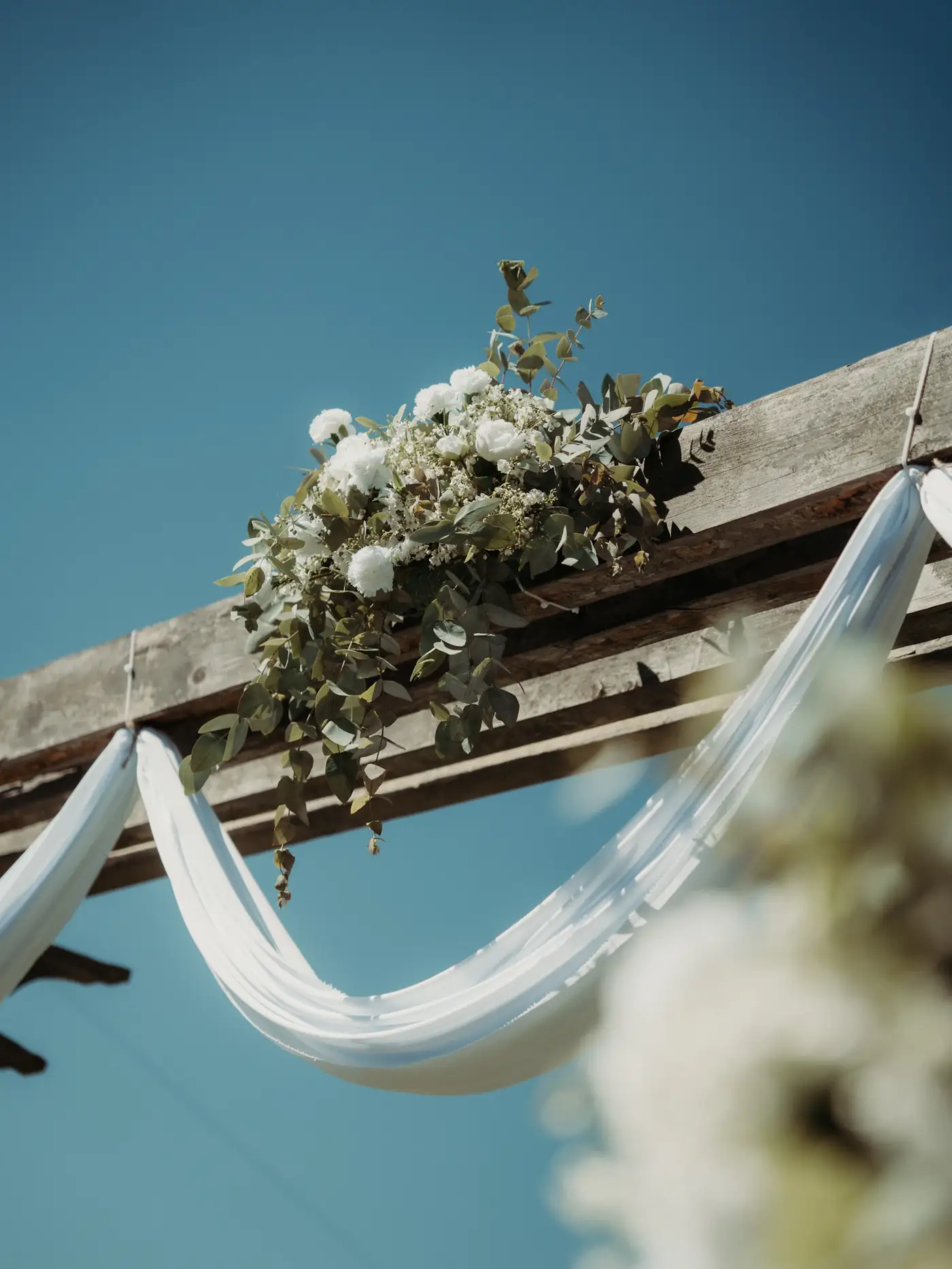 Floral arch draped in white fabric under a blue sky