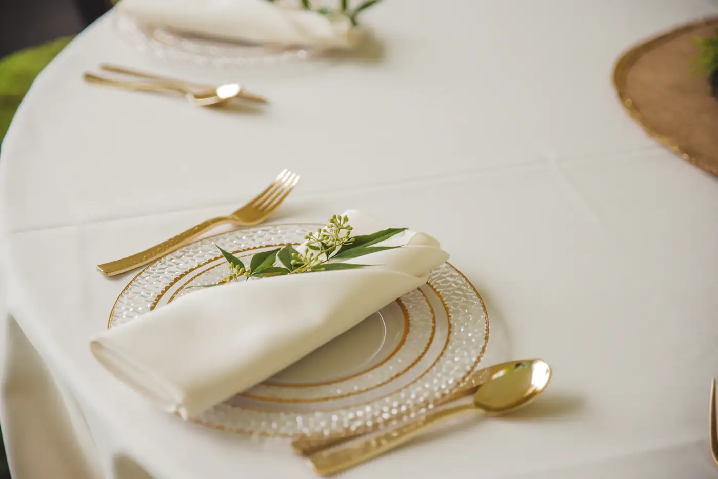 Place setting with a white napkin, gold cutlery and a sprig of green