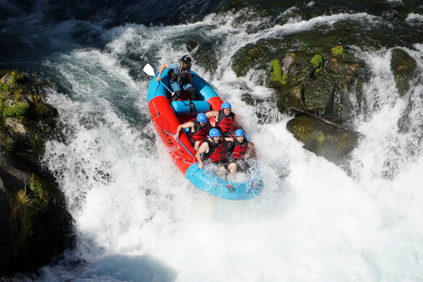 Rafters plunging down a steep rapid in a blue raft